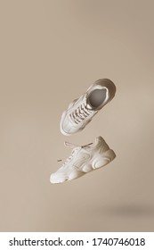 Modern women's sneakers of light color flying on a beige background. Stylish fashionable minimalism, levitation shoes, creative layout. Vertical with copy space for text.