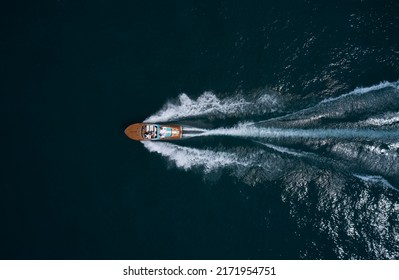 Modern wooden boat in a classic design, moving on water, aerial view. Luxurious wooden boat with people moves on dark water top view. Italian classic wooden boat fast movement on the water top view.