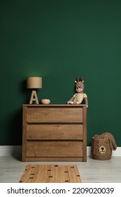 Modern Wooden Chest Of Drawers With Lamp And Toy Near Green Wall Indoors