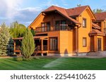 Modern wooden eco house villa facade luxury big house. Timber cottage with with green lawn water sprinkler, paved footpath and blue sky background. Landscaping design, garden watering and maintenance