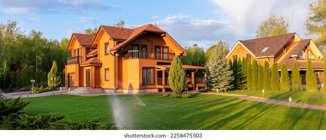 Modern wooden eco house villa facade luxury big house. Timber cottage with with green lawn water sprinkler, paved footpath and blue sky background. Landscaping design, garden watering and maintenance
