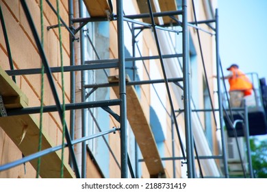 Modern wooden and metal scaffolding next to outer wall and windows of multi-storey building. Against the background of worker-plasterer in telehandler work platform. Blur and selective focus. Daylight - Shutterstock ID 2188731419
