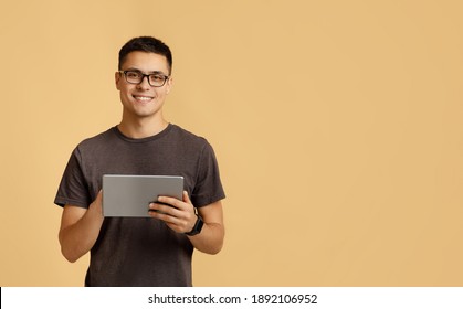 Modern work, social media and online communication. Attractive happy young male student in glasses, with smart watch typing in digital tablet, isolated on beige background, studio shot, free space - Shutterstock ID 1892106952