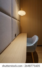 A modern work or study area with a light wood table, gray chairs, round pendant lights, and fabric and wood paneled walls creates a comfortable space.