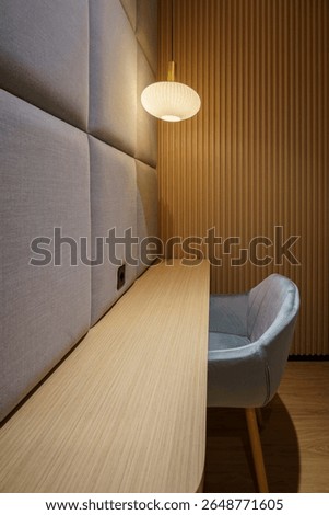 A modern work or study area with a light wood table, gray chairs, round pendant lights, and fabric and wood paneled walls creates a comfortable space.