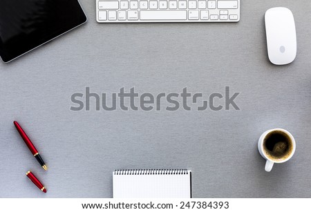 Modern working place on grey wood table. From above view on the well equipped working place surrounded with tablet PC, computer mouse and keyboard, red pen, blank notepad and cup of fresh coffee