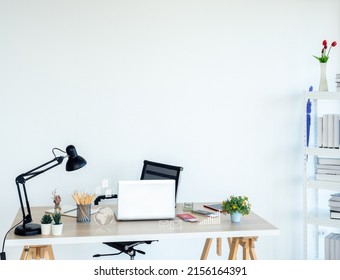 Modern Workplace With Business Icon Virtual Near Laptop Computer, Pencil, Notebook Table Lamp, Cash, Credit Card And Passport On Wood Desk Near The Bookshelf On White Wall Background With Copy Space.