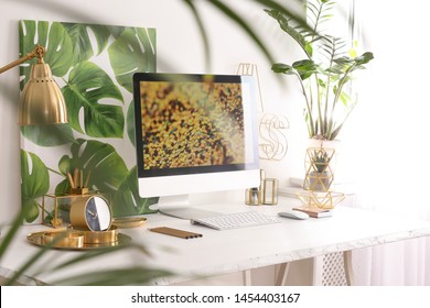 Modern workplace with computer and golden decor on desk near wall. Stylish interior design
