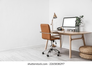 Modern workplace with computer, headphones and microphone near light wall