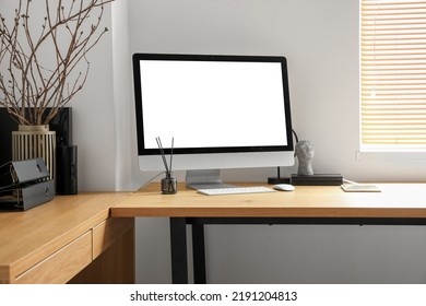 Modern workplace with computer, tablet and tree branches in vase near light wall