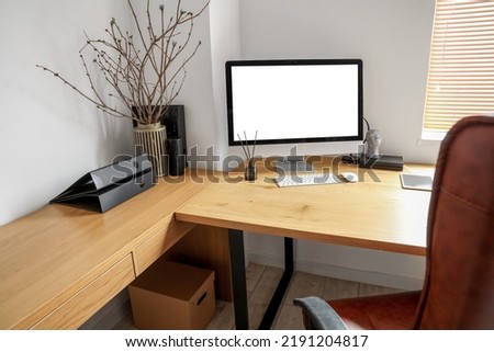 Modern workplace with computer, tablet and tree branches in vase near light wall