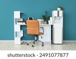 Modern workplace with paper cups and water cooler near blue wall in office