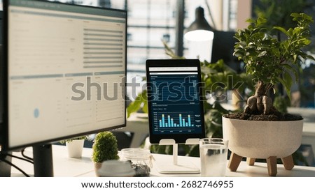 Modern workspace with key performance indicators data on display in bright office environment with potted plants. PC and tablet on desk with accounting figures displayed on screen, close up shot