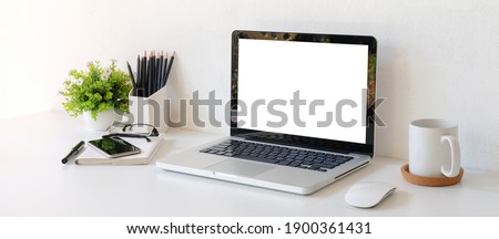 Modern workstation with mock up laptop computer, mobile phone, stationery, coffee cup and plant on white table
