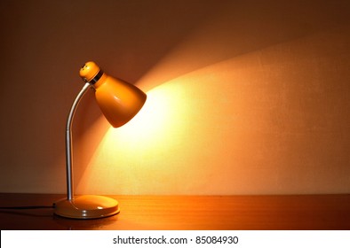 Modern Yellow Luminous Desk Lamp On The Table Near Wall With Beam Of Light