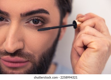 Modern young Caucasian man applying eye cosmetics