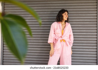 Modern Young Caucasian Woman With Smile On Face Looks Outdoors By Grey Wall. Brunette With Bob Haircut Wears Pink Shirt And Pants. Concept Of Urban Living 