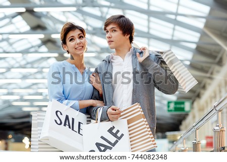 Modern young couple carrying paperbags while walking down large mall on black friday