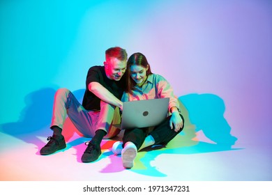 Modern young couple girl and guy working on laptop or shopping online. Colored neon studio light - Powered by Shutterstock