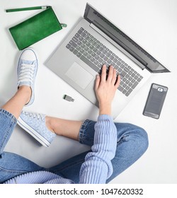 A Modern Young Girl Sits On A White Floor And Use A Laptop. Generation Z. The Concept Of Freelancing. Working Space. Top View.