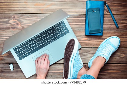 A Modern Young Girl Sits On A Wooden Floor And Enjoys A Laptop. Generation Z. The Concept Of Freelancing. Working Space. Top View.