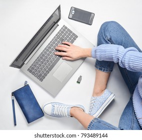 A Modern Young Girl Sits On A White Floor And Use A Laptop. Generation Z. The Concept Of Freelancing. Working Space. Top View.