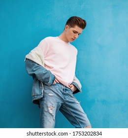 Modern Young Man In Stylish Denim Casual Wear From New Youth Collection Posing On Blue Background In City. Attractive Glamorous Guy Stands Looking Down Near Vintage Wall In Street. Summer Style.