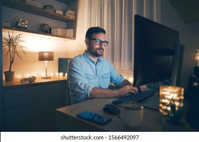 Modern young man working remotely from home at night. 