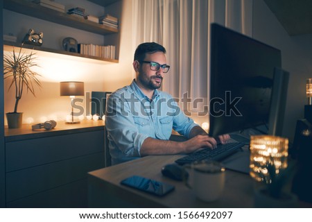 Modern young man working remotely from home at night. 