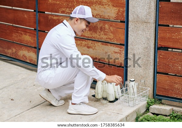 Modern young milkman\
delivering milk and bringing back empty glass bottles, horizontal\
high angle shot