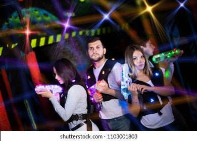 Modern young people playing laser tag on dark labyrinth in bright beams of laser pistols 