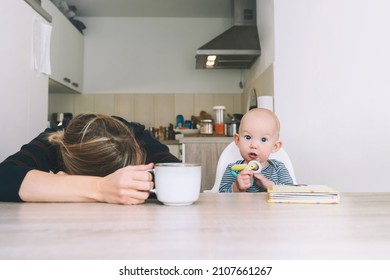 Modern Young Tired Mom And Little Child After Sleepless Night. Exhausted Woman With Baby Is Sitting With Coffee In Kitchen. Life Of Working Mother With Baby. Postpartum Depression On Maternity Leave.