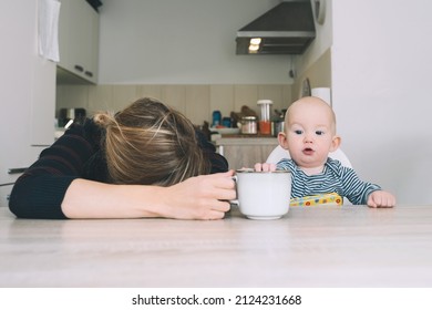 Modern Young Tired Mom And Little Child After Sleepless Night. Exhausted Woman With Baby Is Sitting With Coffee In Kitchen. Life Of Working Mother With Baby. Postpartum Depression On Maternity Leave.