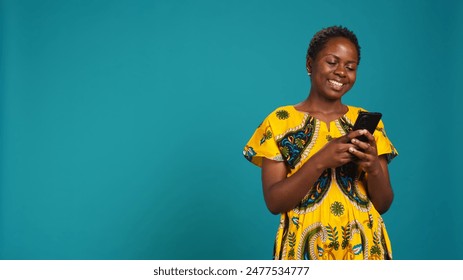 Modern young woman browses online websites on her phone, standing against blue background. Cheerful satisfied girl checks her texts on social media, using a smartphone in studio. Camera B. - Powered by Shutterstock