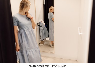  Modern young woman has opportunity to evaluate how she is wearing dress in fitting room of clothing store. Organization of sales process in supermarkets. Fashionable clothes. Shopping and pleasure. 
