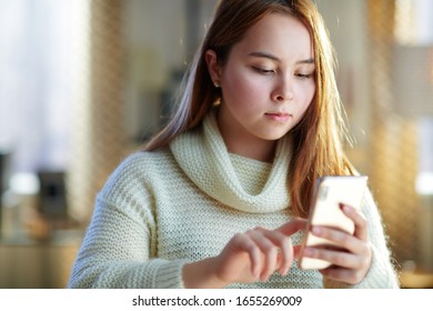 Modern Young Woman With Red Hair In White Sweater With Smartphone Driving The Growth Of Social Media In The Modern House In Sunny Winter Day.