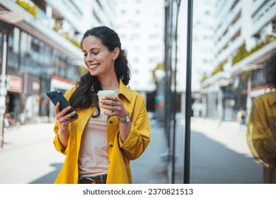 Modern young woman walking on the city street texting and holding cup of coffee. Business woman holding smartphone and looking away outdoors. Beautiful woman spending time in the city  - Powered by Shutterstock