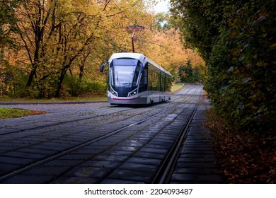 A modern-style tram goes out of a dense forest in autumn colours, Moscow, Russia