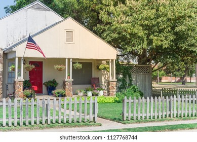 Modest house with chimney in historic downtown district of Irving, Texas, USA. Classic wooden fence with well-groomed landscape, haning flower pots, big tree and proudly American flag waving