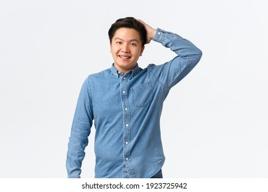 Modest Smiling Asian Man, Blushing As Making Good Deed, Scratching Head Confused And Awkward, Standing Cute Over White Background. Nice Guy Talking To Pretty Lady