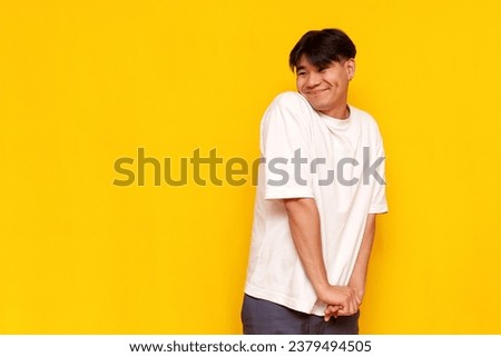 modest young asian guy in a white t-shirt is shy and embarrassed on a yellow isolated background, touched korean guy happy looking aside at copy space