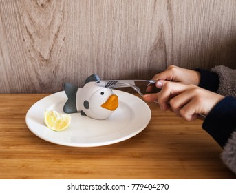 Modified Food Concept. A Child Is Eating With A Knife And Fork A Synthetic Fish Presented On A White Plate. Close Up Baby's Hands And Plate.