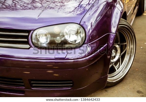 Modified headlights of tuned purple candy colored\
lowrider. Stance custom car with a forged polished wheels stays on\
a street