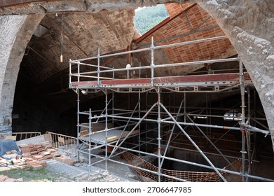 Modular scaffolding framework inside an old, abandoned factory ruin undergoing reconstruction and safety maintenance. Brick arch and collapsed ceiling