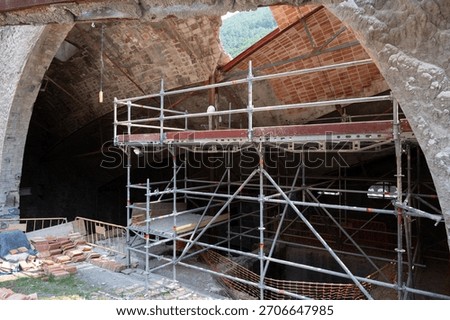 Modular scaffolding framework inside an old, abandoned factory ruin undergoing reconstruction and safety maintenance. Brick arch and collapsed ceiling
