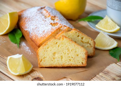 Moist lemon pound cake on parchment on rustic wooden background with slices of lemon and cup of tea on plate. Delicious breakfast, traditional tea time treat. Reciepe of English lemon pie loaf.