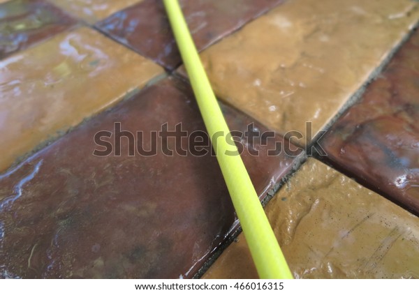 Moist modern concrete parking tiles crossed by a\
yellow garden hose