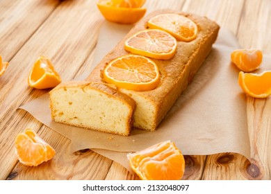 Moist Orange Fruit Pound Cake On Parchment On Rustic Wooden Background With Slices Of Orange. Delicious Breakfast, Traditional English Tea Time. Reciepe Of Orange Pie Loaf.