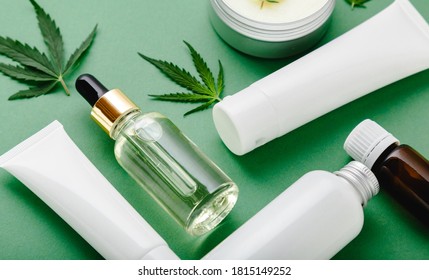 Moisturizing Cream, Serum, Lotion, CBD Oil, Essential Oil Cannabis Leaves. Set Of Hemp Skin Care Cosmetics In White Mockup Packaging. Flat Lay On Green Background