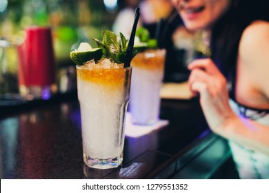 Mojito Classic Cocktails On Bar. Close-up Cold Cocktail With Crushed Ice, Mint And Slice Of Lime With Burning Sugar Cube On Glass. Young Happy Pretty Girl Drinking Cocktails At Bar Counter In Bar.